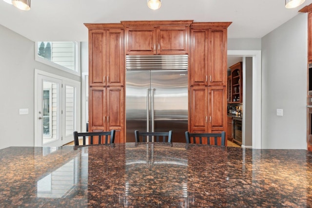 kitchen with dark stone countertops, beverage cooler, a breakfast bar, and built in refrigerator