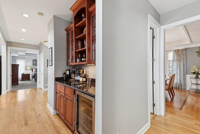 bar with beverage cooler, sink, light hardwood / wood-style flooring, and dark stone countertops