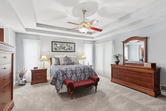 carpeted bedroom featuring multiple windows, a tray ceiling, and ceiling fan