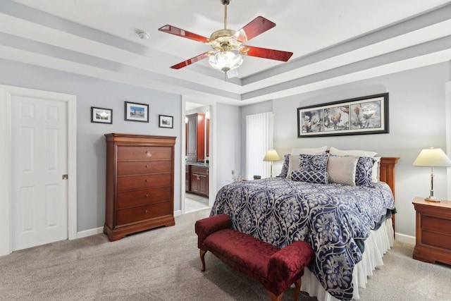 carpeted bedroom featuring ceiling fan, a tray ceiling, and ensuite bath