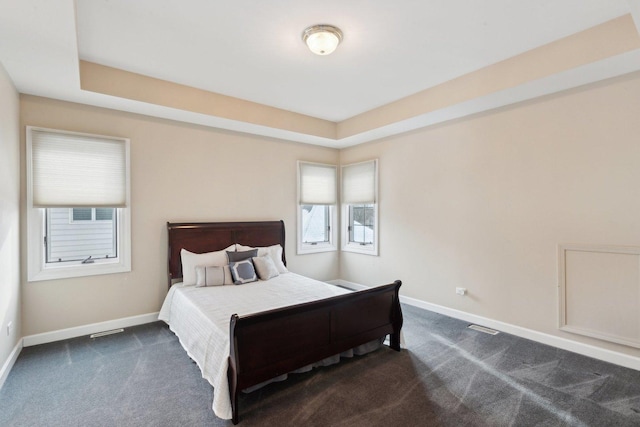 bedroom with dark colored carpet and a tray ceiling