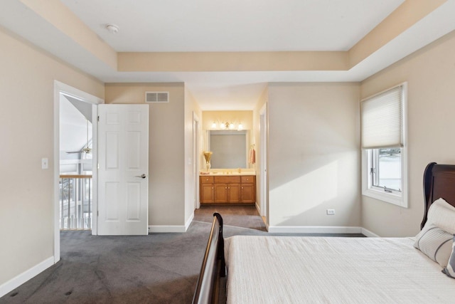 bedroom with connected bathroom, a tray ceiling, and dark colored carpet