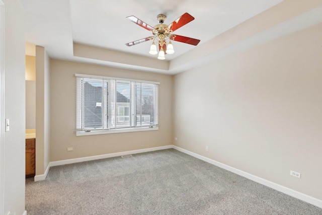 empty room with ceiling fan, a raised ceiling, and carpet floors