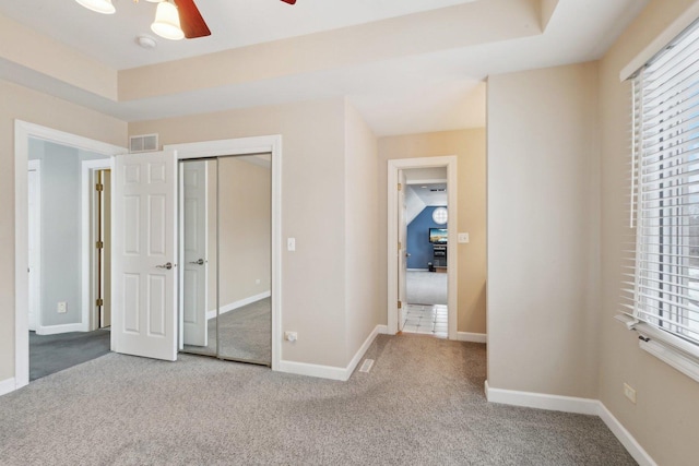 unfurnished bedroom featuring multiple windows, a tray ceiling, carpet floors, and a closet