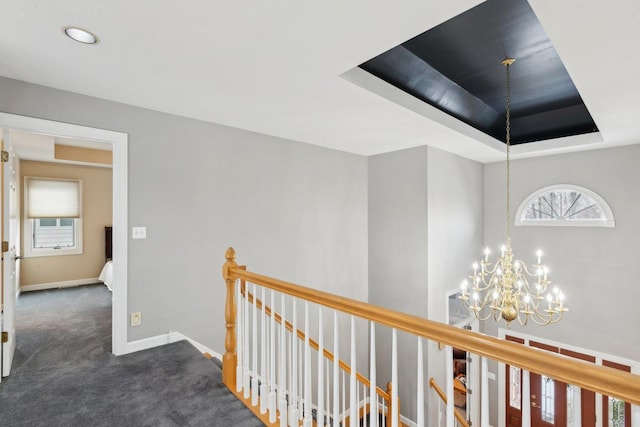 hall featuring a wealth of natural light, a raised ceiling, a chandelier, and dark colored carpet