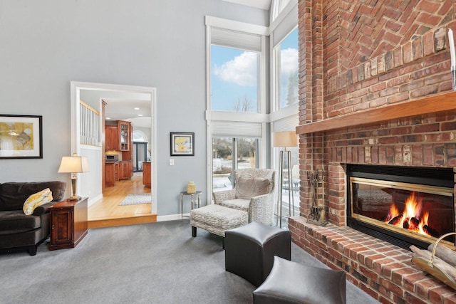 living area featuring a towering ceiling, a fireplace, and carpet