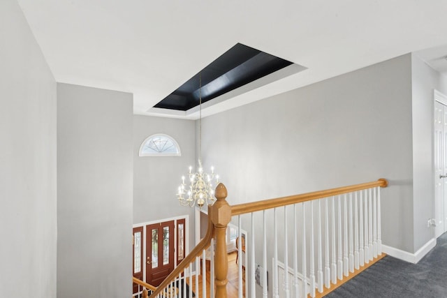 hall with a chandelier, a raised ceiling, and dark colored carpet