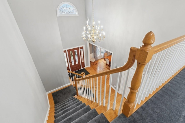 stairway featuring a towering ceiling, hardwood / wood-style floors, and a notable chandelier