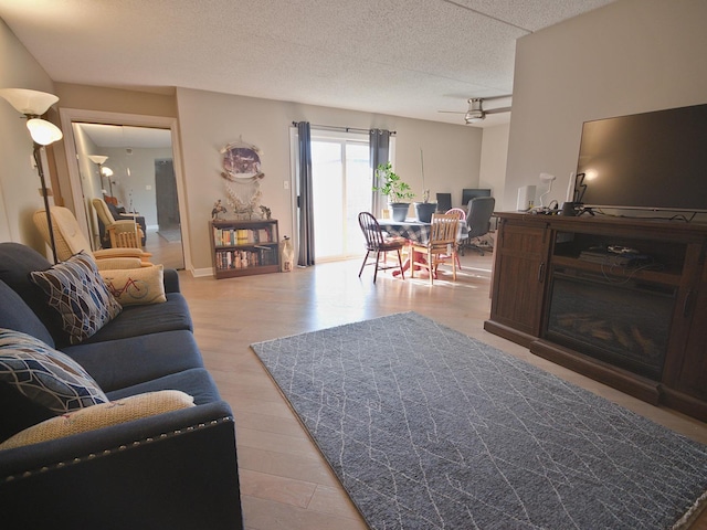 living room with ceiling fan, light hardwood / wood-style floors, and a textured ceiling