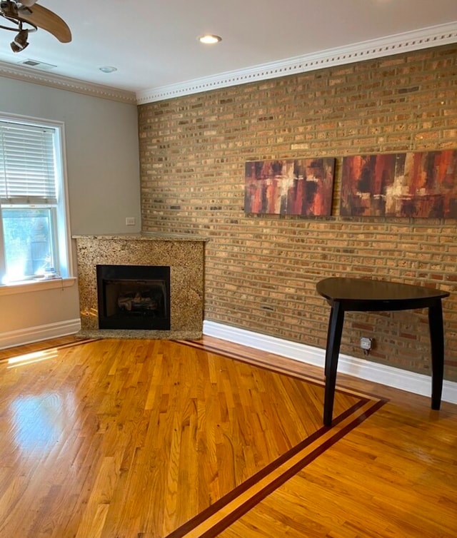 interior space featuring ceiling fan, wood-type flooring, ornamental molding, and brick wall