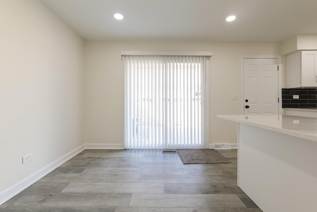 kitchen with decorative backsplash, white cabinetry, light hardwood / wood-style flooring, and light stone counters