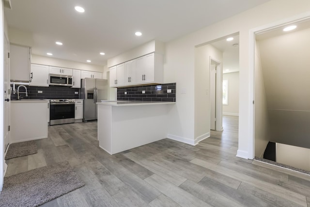 kitchen with white cabinets, light hardwood / wood-style flooring, appliances with stainless steel finishes, tasteful backsplash, and kitchen peninsula