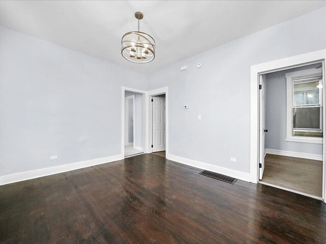 empty room with dark hardwood / wood-style flooring and a chandelier