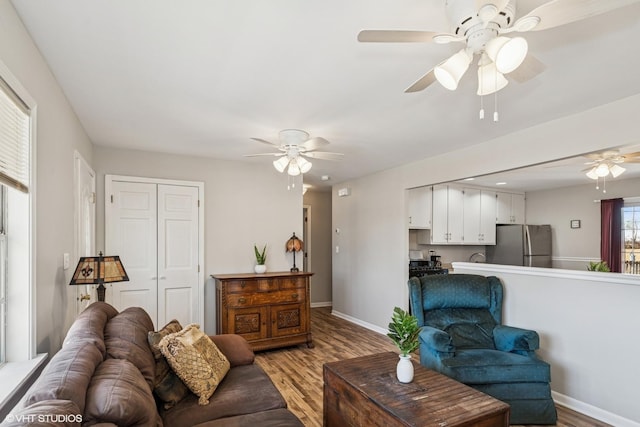 living room featuring light wood-style floors, baseboards, and ceiling fan