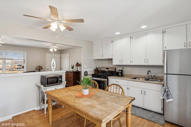 kitchen with a sink, ceiling fan, stainless steel appliances, white cabinets, and light wood-style floors