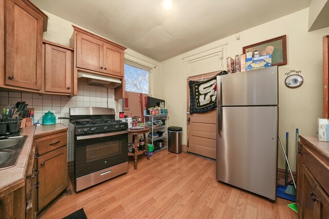 kitchen with sink, backsplash, appliances with stainless steel finishes, and light hardwood / wood-style flooring