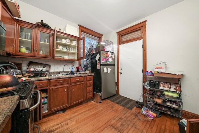 kitchen with light stone countertops, sink, stainless steel appliances, backsplash, and light wood-type flooring