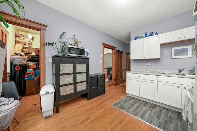 kitchen featuring white stove, sink, light hardwood / wood-style floors, light stone counters, and white cabinetry