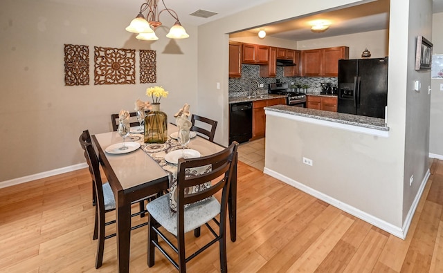 dining space with light wood-type flooring, sink, and a chandelier