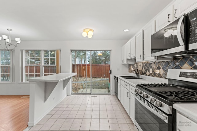 kitchen with sink, white cabinetry, hanging light fixtures, appliances with stainless steel finishes, and backsplash