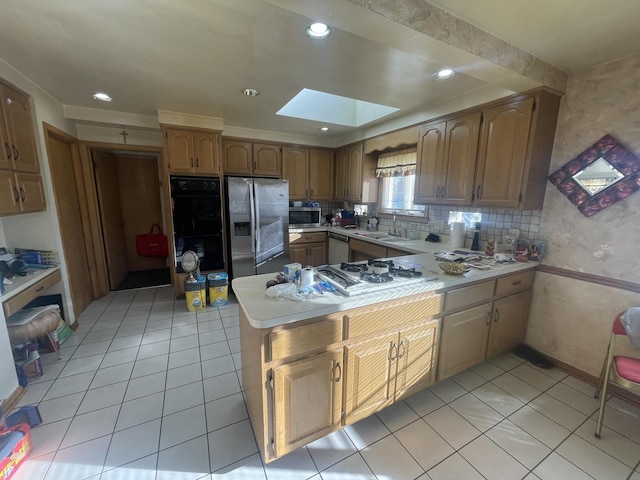 kitchen featuring a skylight, kitchen peninsula, light tile patterned floors, and appliances with stainless steel finishes