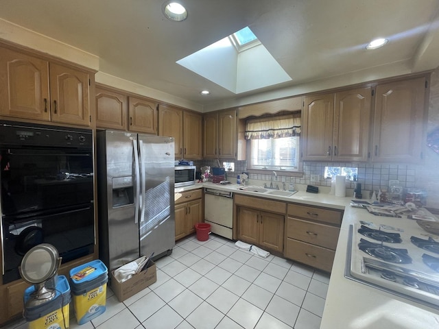 kitchen with a skylight, sink, stainless steel appliances, backsplash, and light tile patterned floors