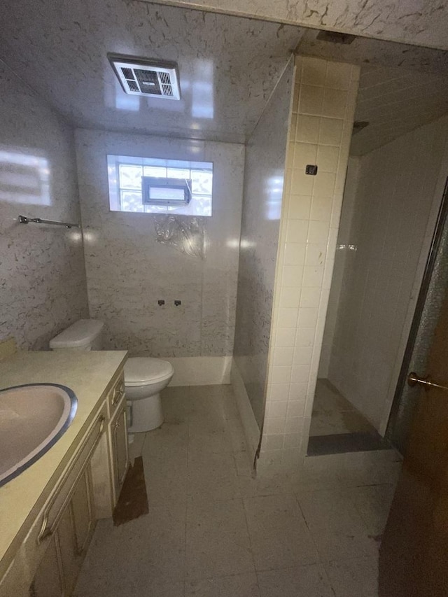 bathroom with tile patterned flooring, a shower, toilet, vanity, and tile walls