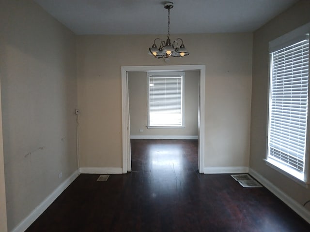 unfurnished dining area with dark wood-type flooring, a healthy amount of sunlight, and a notable chandelier