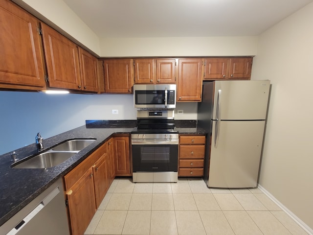 kitchen with sink, light tile patterned floors, stainless steel appliances, and dark stone counters