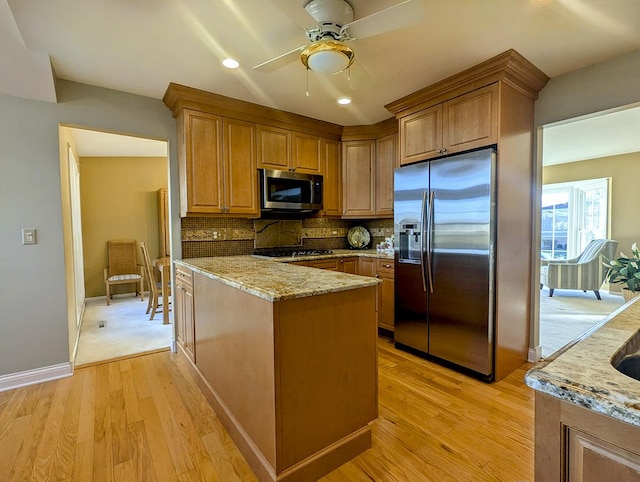 kitchen featuring appliances with stainless steel finishes, backsplash, light hardwood / wood-style floors, and light stone counters