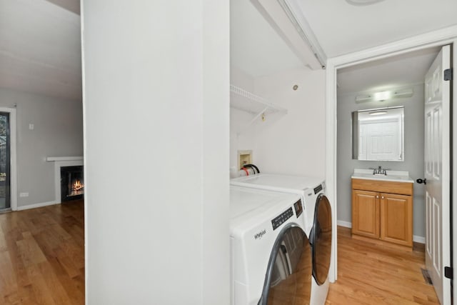 laundry area featuring washing machine and dryer, sink, and light hardwood / wood-style floors