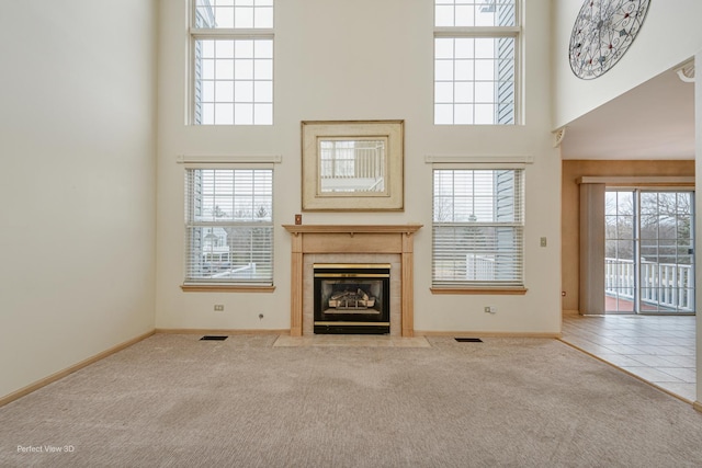 unfurnished living room featuring a tile fireplace, a high ceiling, light colored carpet, and a healthy amount of sunlight