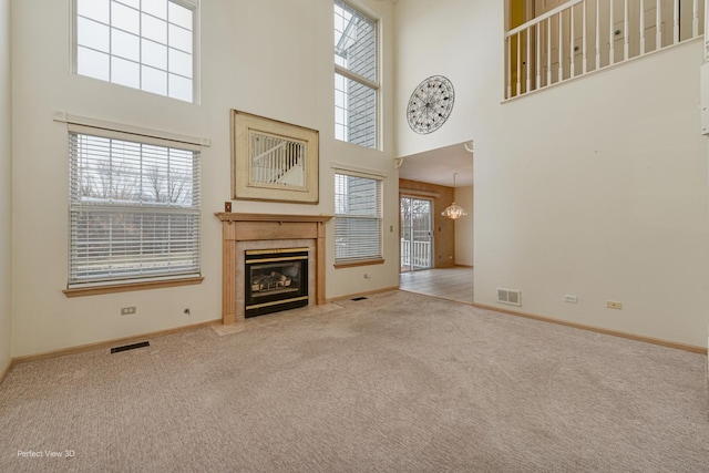 unfurnished living room with a healthy amount of sunlight, light colored carpet, a fireplace, and a high ceiling