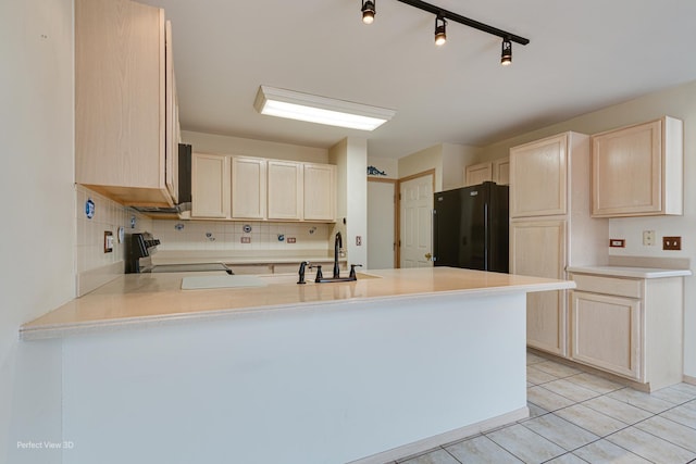 kitchen featuring kitchen peninsula, backsplash, black fridge, sink, and electric stove