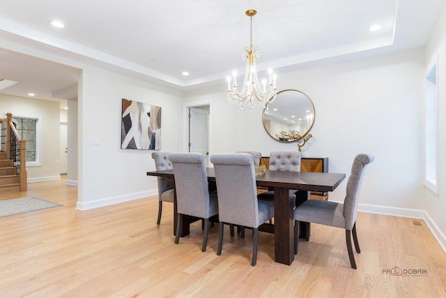 dining area featuring light hardwood / wood-style floors, a raised ceiling, and a chandelier