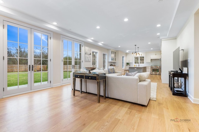 living room featuring sink, an inviting chandelier, light hardwood / wood-style floors, and french doors