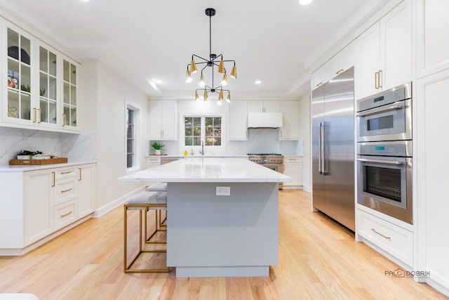 kitchen featuring premium appliances, light hardwood / wood-style floors, white cabinets, a kitchen island, and decorative light fixtures