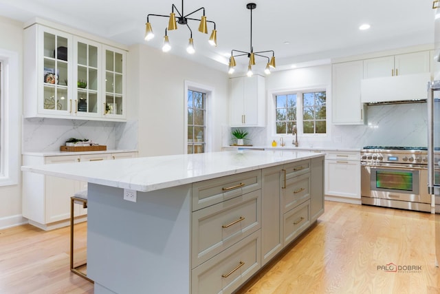 kitchen featuring decorative light fixtures, high end stove, white cabinetry, a center island, and light stone countertops