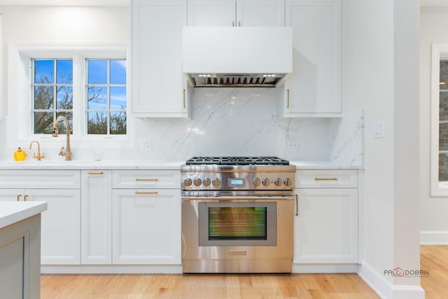 kitchen with premium range hood, white cabinetry, backsplash, high end range, and light wood-type flooring