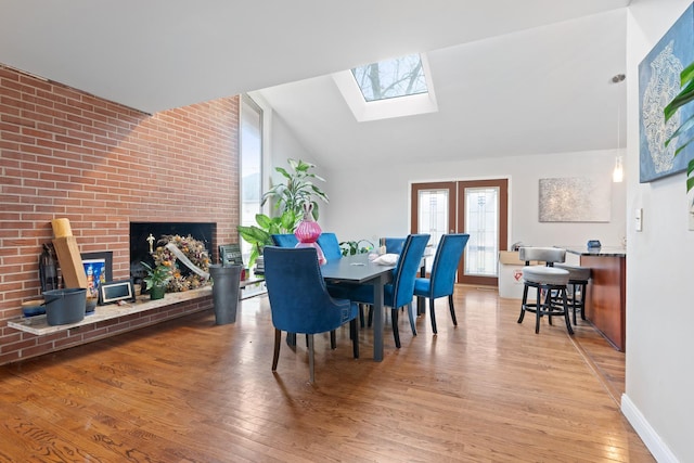 dining space with a brick fireplace, lofted ceiling with skylight, and light hardwood / wood-style flooring