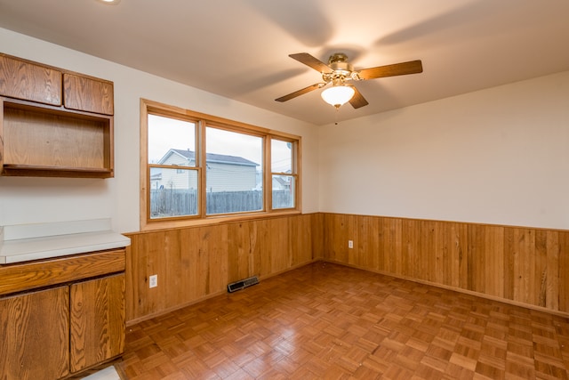 interior space with ceiling fan, wood walls, and light parquet flooring