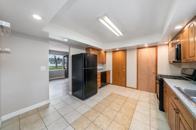 kitchen featuring black appliances, a raised ceiling, sink, built in desk, and light tile patterned flooring