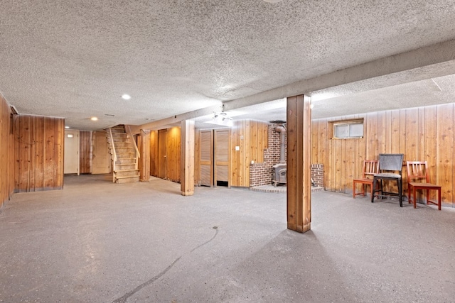 basement with wood walls, a wood stove, and a textured ceiling