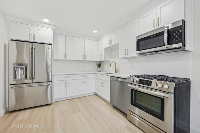 kitchen featuring appliances with stainless steel finishes, light wood-type flooring, backsplash, sink, and white cabinets