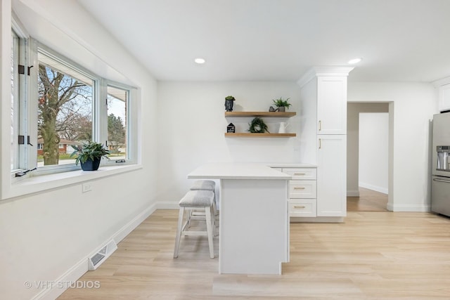 kitchen featuring a kitchen breakfast bar, light hardwood / wood-style floors, white cabinetry, and stainless steel refrigerator with ice dispenser