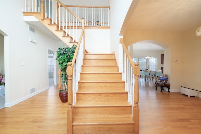 staircase with wood-type flooring, an inviting chandelier, and baseboard heating