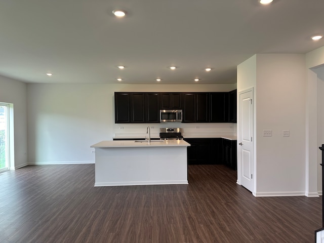 kitchen with a center island with sink, sink, dark wood-type flooring, and stainless steel appliances