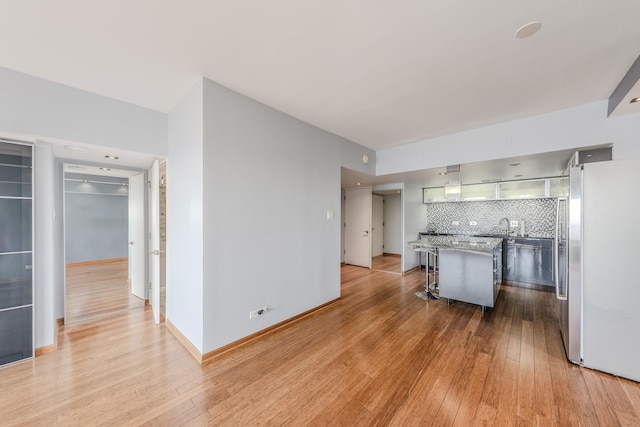 kitchen featuring tasteful backsplash, a kitchen breakfast bar, stainless steel refrigerator, and light wood-type flooring