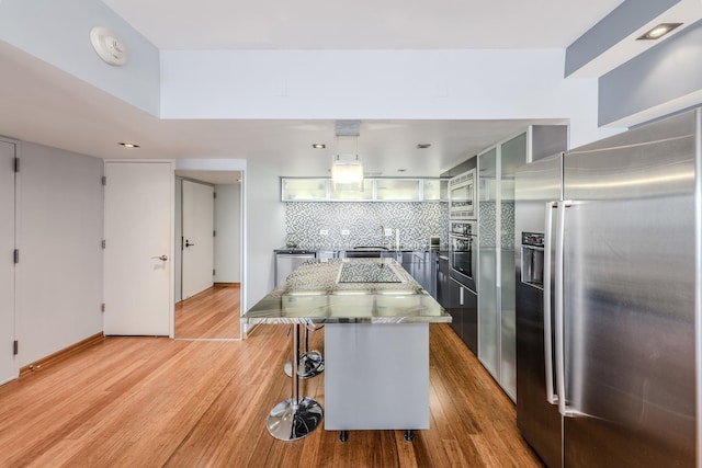 kitchen with a breakfast bar area, stone counters, appliances with stainless steel finishes, a center island, and light wood-type flooring