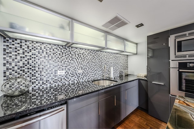 kitchen with sink, dark stone counters, dark hardwood / wood-style floors, stainless steel appliances, and backsplash